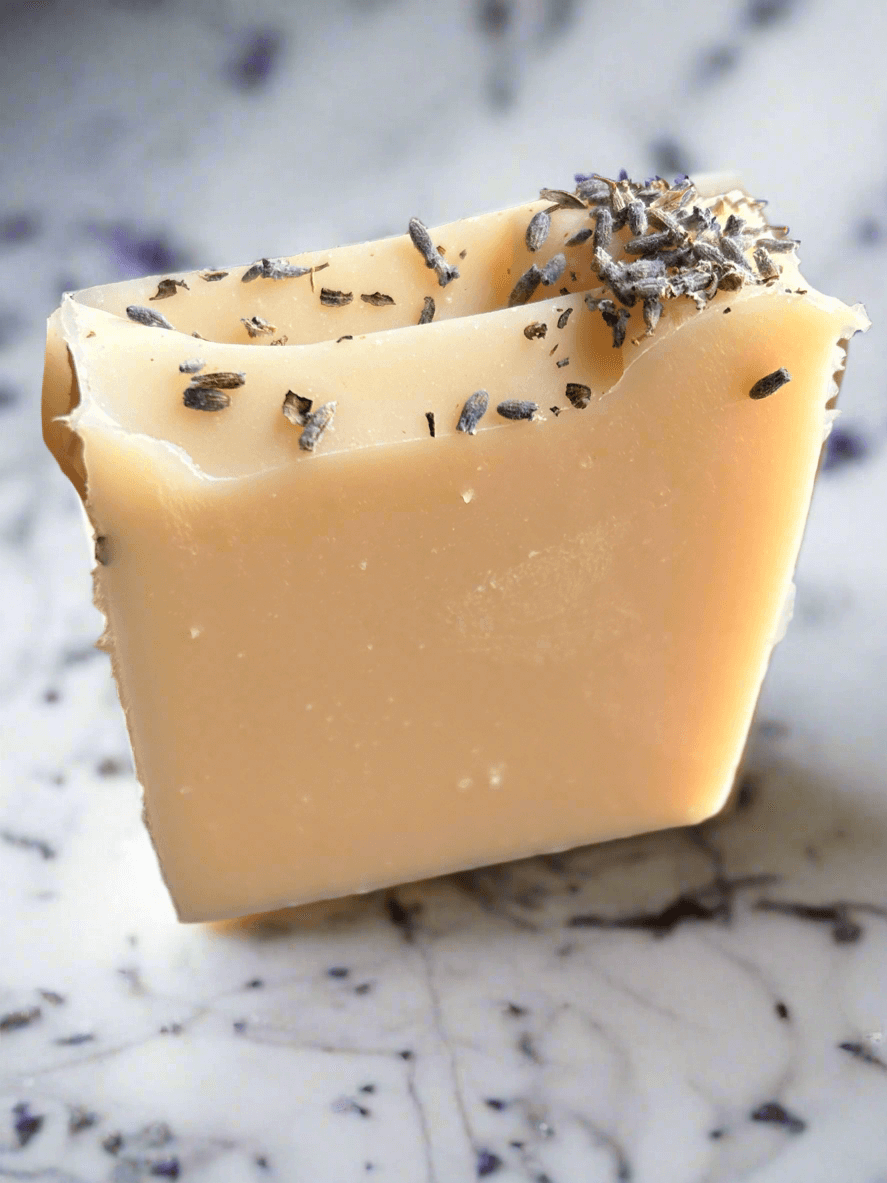 Handcrafted Lavender Goat Milk Soap bar with lavender pieces on marble background.