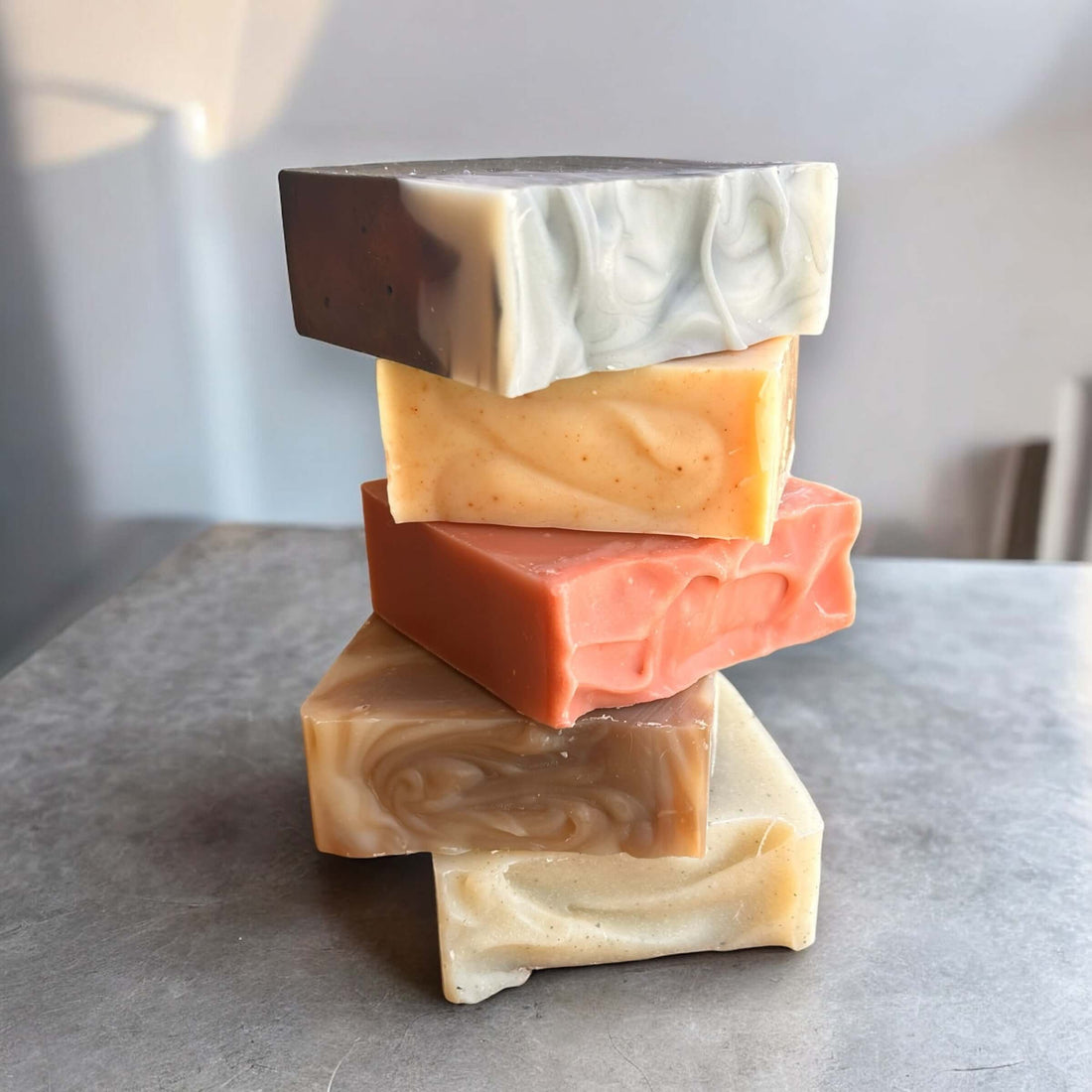 Does Bar Soap Really Kill Germs? Stack of colorful handmade bar soaps on a gray surface.