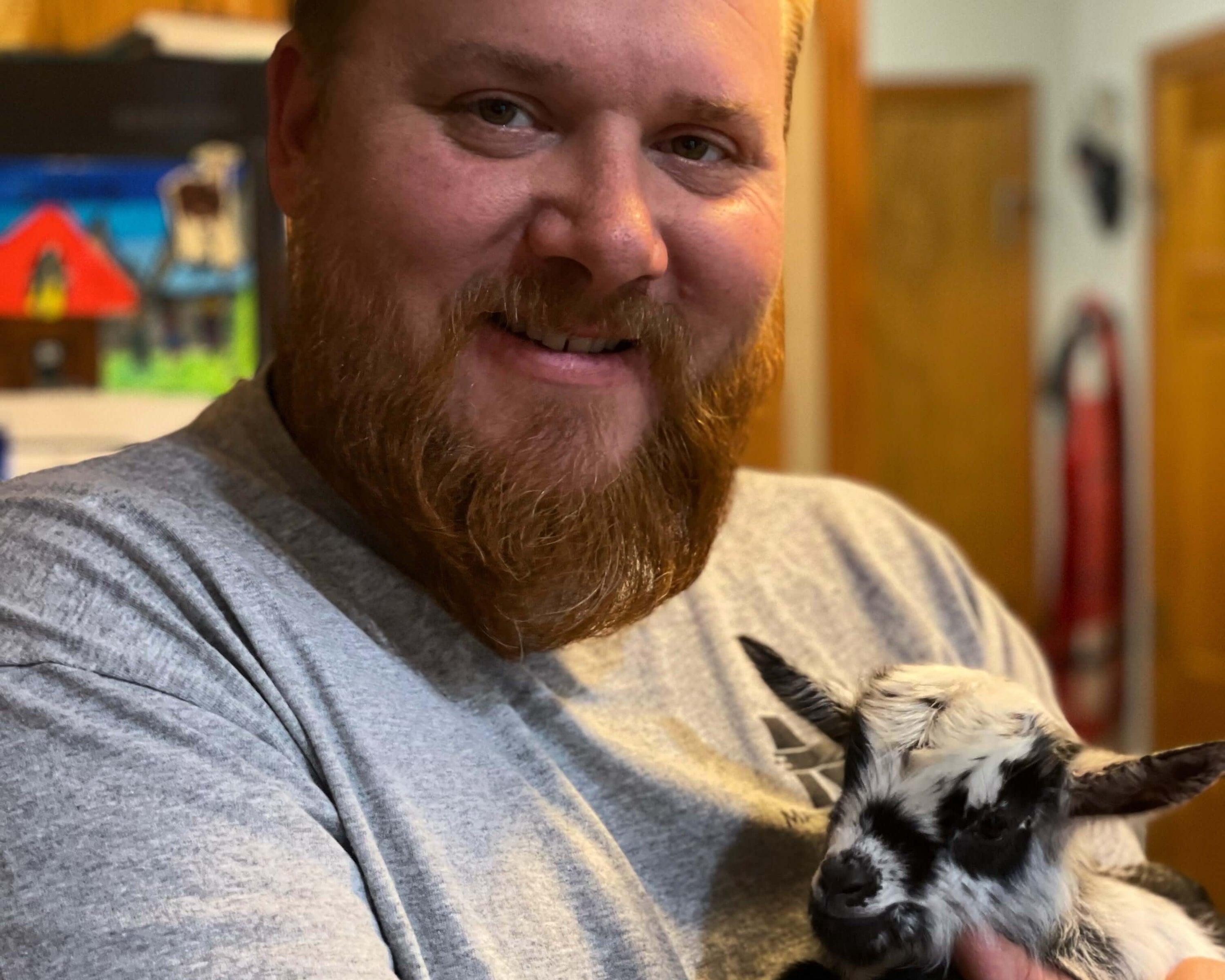 A smiling man with a beard holds a cute black and white goat, showcasing bonding with animals.