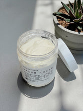 Jar of cream with a label on a gray surface next to a potted plant