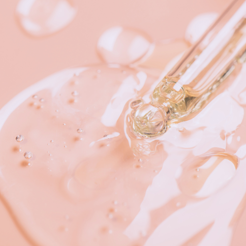Close-up of a dropper with liquid being applied to a pink surface