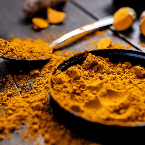 Turmeric powder in black measuring spoons on a wooden surface