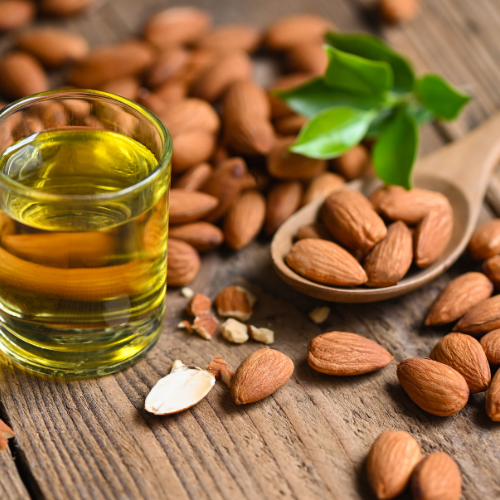 Glass of almond oil with almonds on a wooden surface