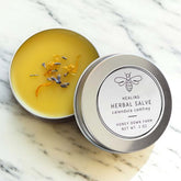 Calendula Herbal Salve in a silver tin, infused with herbs, resting on a marble surface.