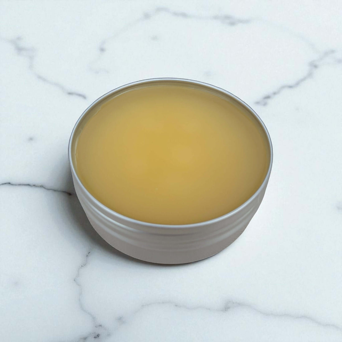 Comfrey Mint Herbal Chest Balm in a portable tin on a marble surface.