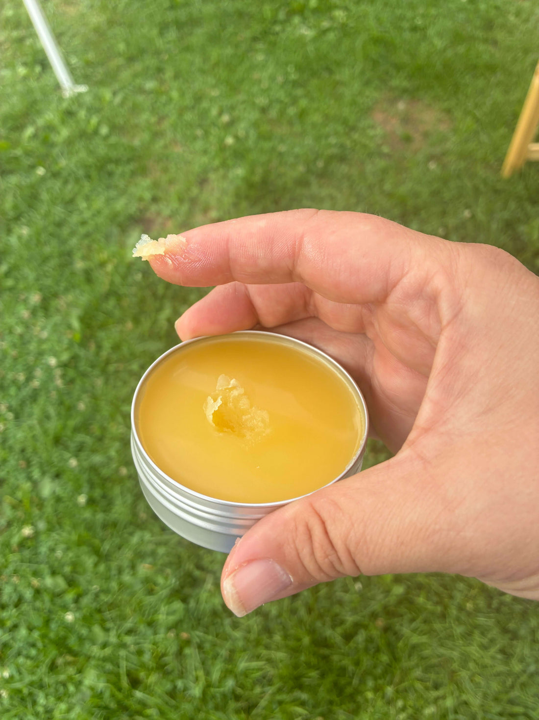 Person holding a tin of Comfrey Mint Herbal Chest Balm with finger dipped in the balm outdoors.