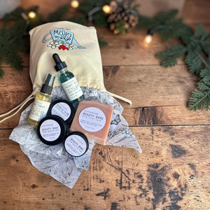The Glow Ritual gift set laid out on gift tissue with its cotton gift bag, surrounded by pine branches.
