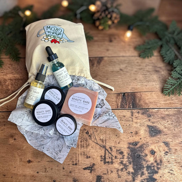 The Glow Ritual gift set laid out on gift tissue with its cotton gift bag, surrounded by pine branches.