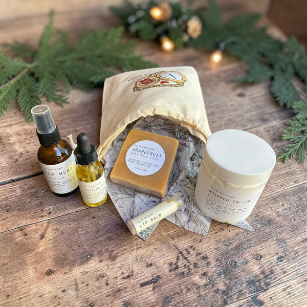 Winter Skin Rescue gift set tucked into its cotton gift bag with pine branches on a wooden table.