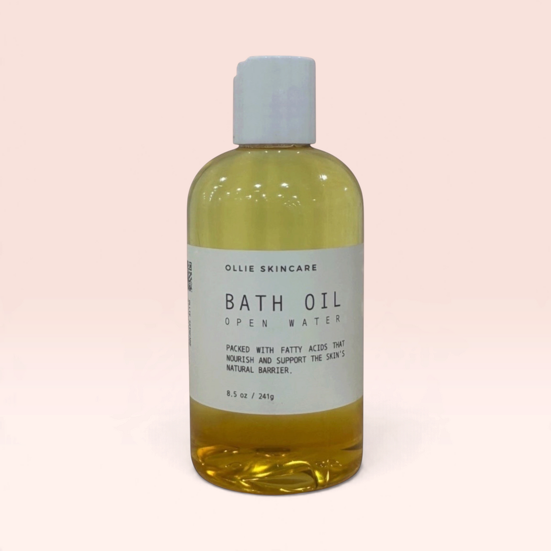 OLLIE SKINCARE moisturizing bath oil in a clear 8.5 oz bottle with a white cap against a soft pink background.