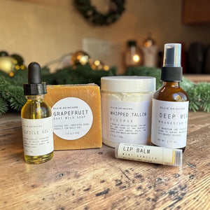 Close-up of the Winter Skin Rescue products: cuticle oil, Grapefruit goat milk soap, Whipped Tallow, magnesium oil and lip balm.
