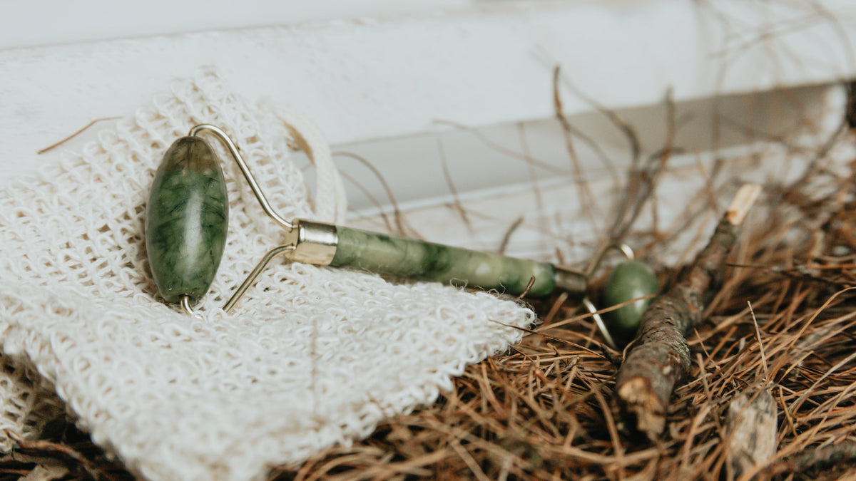 Jade face roller on a white cloth with pine needles