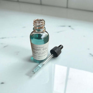 Night Facial Oil in a glass dropper bottle on a marble surface with a dropper top.