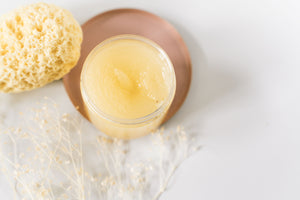 OLLIE SKINCARE nourishing makeup removing balm in a clear jar with a natural sea sponge on a soft pink background.