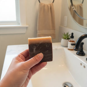 OLLIE SKINCARE Tipsy Goat Soap, a handmade two-tone brown goat milk and beer bar soap held in a bathroom setting.
