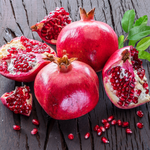 Pomegranates on a wooden surface with some cut open to reveal seeds.