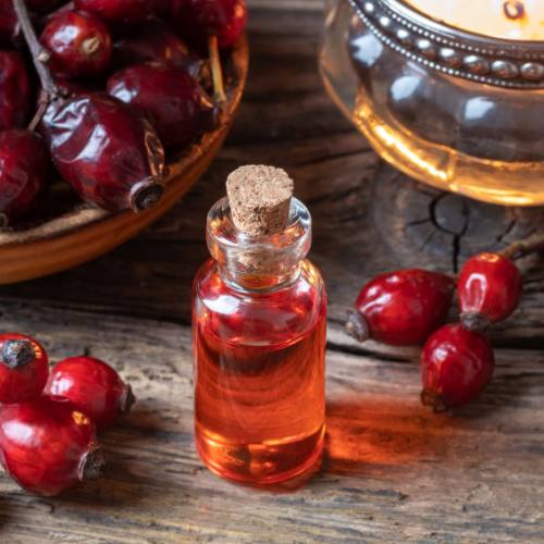 Glass bottle with cork stopper surrounded by red berries on a wooden surface
