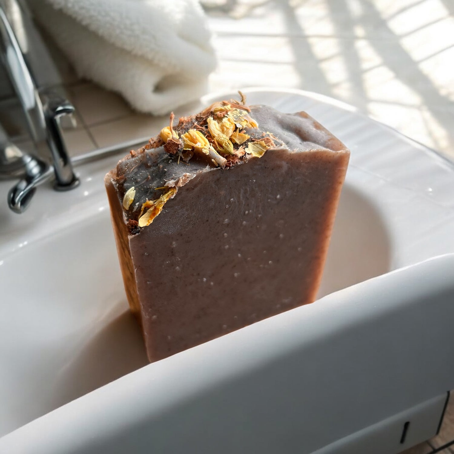Roughcut Goat Milk Soap bar with flower petals on a sink edge in natural light.